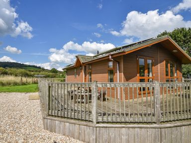 A wooden cabin with a fenced deck and outdoor table set in a rural area at The Hideaway in Eype