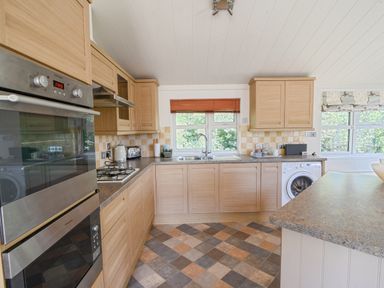 A kitchen with wooden cabinets an oven a gas stove a sink and a washing machine at The Hideaway in Eype