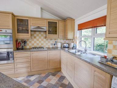 A kitchen with wooden cabinets a gas stove oven microwave double sink and window blinds at The Hideaway in Eype