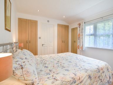 A bedroom with a bed covered in floral bedding two wooden wardrobes a window with curtains and a door at The Hideaway in Eype