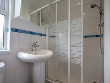 A bathroom with a pedestal sink a mirror cabinet a shower with sliding glass doors and tiled walls at The Hideaway in Eype