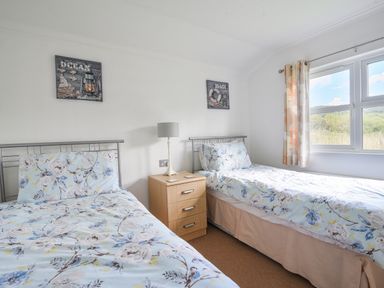 A bedroom with two single beds with floral bedding a wooden nightstand with a lamp and a window at The Hideaway in Eype