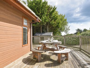 An outdoor wooden deck with a round picnic table set with plates and glasses surrounded by railing and trees at The Hideaway in Eype
