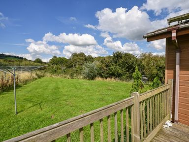 A grassy backyard with a rotary clothesline and wooden deck railing at The Hideaway in Eype