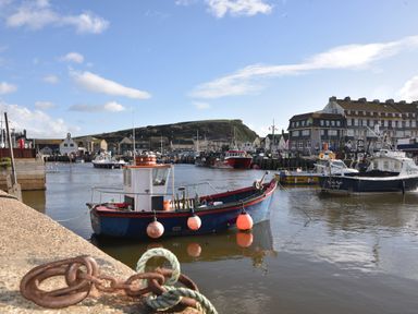 A harbor with several boats docked near buildings and a hill in the background at The Hideaway in Eype