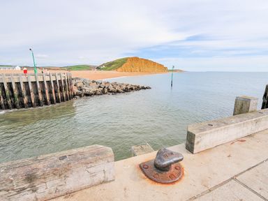 A pier overlooking a rocky coastline and sandy beach with grassy cliffs at The Hideaway in Eype