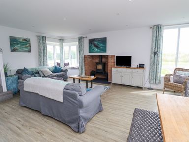 A living room with gray sofas a wood stove a TV on a cabinet and wicker chair at Turning Tide in Beadnell