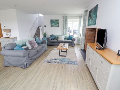 A living room with two sofas a coffee table a TV on a cabinet and a staircase at Turning Tide in Beadnell