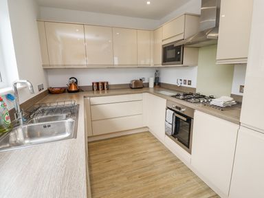 A kitchen with a sink, stove, oven, microwave, kettle, toaster, and cabinets at Turning Tide in Beadnell