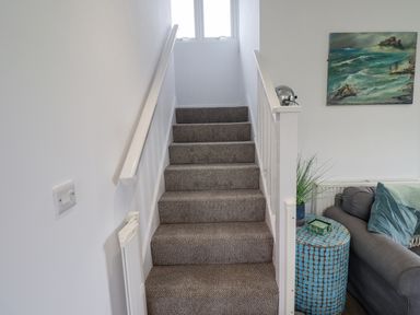 Carpeted staircase with white walls next to a blue side table and a gray sofa at Turning Tide in Beadnell