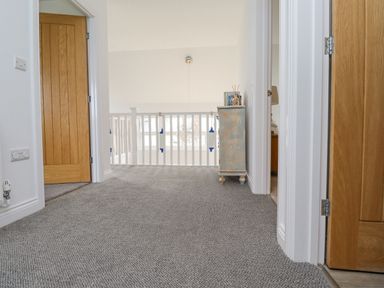 A hallway with gray carpet wooden doors and a small chest at Turning Tide in Beadnell