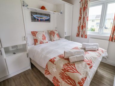 A bedroom with a double bed white and orange bedding and cushions and a window with curtains at Turning Tide in Beadnell