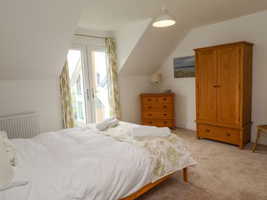 A bedroom with a bed, wooden wardrobe, chest of drawers, lamp, and glass doors at Turning Tide in Beadnell