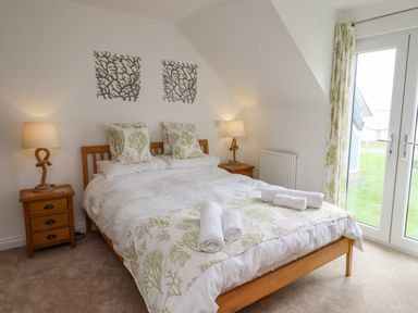 A bedroom with a wooden bed two bedside tables with lamps and a door leading outside at Turning Tide in Beadnell