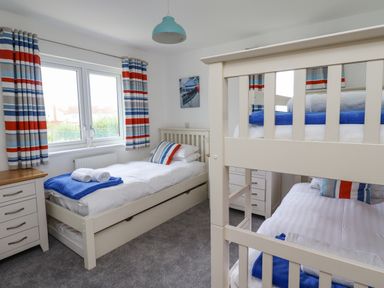 A bedroom with a single bed and bunk beds with striped curtains at Turning Tide in Beadnell