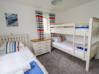 A bedroom with a single bed and bunk beds a chest of drawers and striped curtains at Turning Tide in Beadnell
