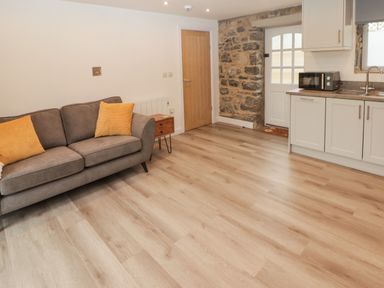 A living area with a gray sofa and yellow pillows next to a kitchen with white cabinets and a wooden door at The Stable in Amroth