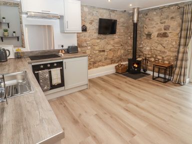 A kitchen with a wood stove on a stone wall and wooden floors at The Stable in Amroth