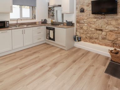 A kitchen with white cabinets a microwave a kettle and toaster a TV on a stone wall and a basket of logs at The Stable in Amroth