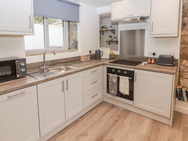 A kitchen with white cabinets a sink microwave toaster oven and kettle at The Stable in Amroth
