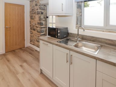 A kitchen with a sink microwave wooden door and stone wall at The Stable in Amroth