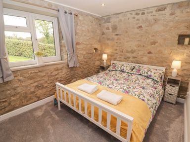 A bedroom with a bed with floral bedding yellow blanket and towels by a stone wall at The Stable in Amroth