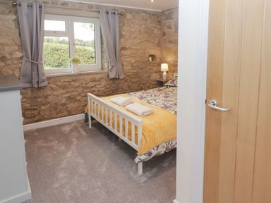 A bedroom with stone walls a bed with floral bedding and a yellow throw and a window with gray curtains at The Stable in Amroth