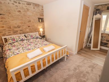 A bedroom with a white bed frame floral bedding two rolled towels nightstand lamp full length mirror and wooden door at The Stable in Amroth