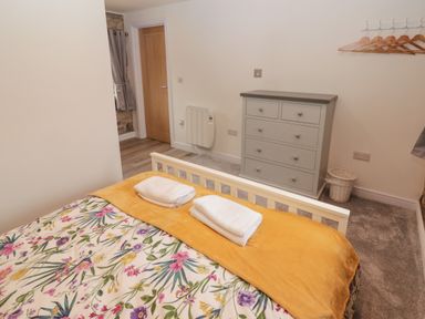 A bedroom with a floral bedspread and yellow blanket on a bed a gray chest of drawers and a wooden door at The Stable in Amroth
