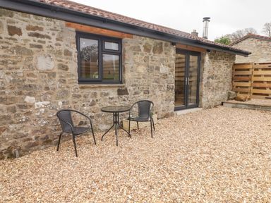 A stone building exterior with two black chairs and a small round table on a gravel surface at The Stable in Amroth