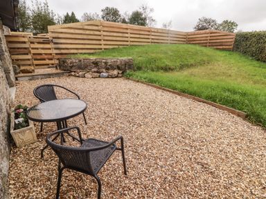 A gravel patio with two chairs and a table next to a lawn and wooden fence at The Stable in Amroth