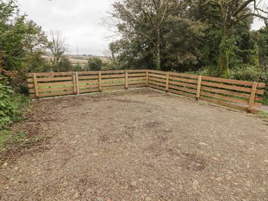 A gravel area enclosed by a wooden fence next to trees and greenery at The Stable in Amroth