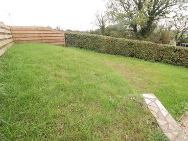A fenced grassy backyard with a stone path and hedge at The Stable in Amroth