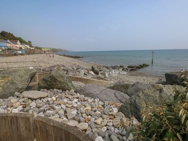 A rocky beach with houses along the shore and a calm sea at The Stable in Amroth