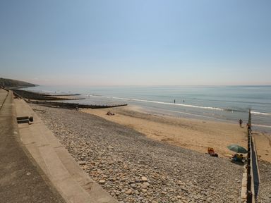 A beach with pebbles and sand next to a sea with wooden groynes and a concrete promenade at The Stable in Amroth