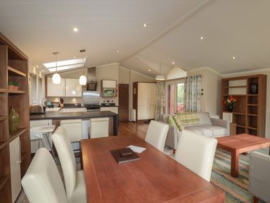 An open plan living space with a dining table and chairs kitchen area with island and stools and a sitting area with sofas and bookshelves at Haven Lodge in Bossiney Bay near Tintagel