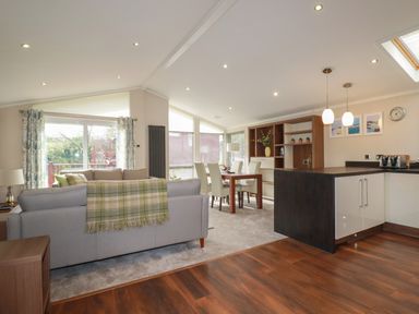 An open living room and kitchen area with a sofa a dining table and modern kitchen at Haven Lodge Bossiney Bay near Tintagel
