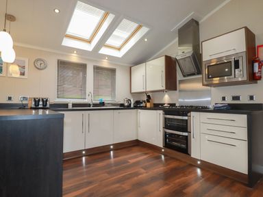 A kitchen with white cabinets wooden floor skylight windows and stainless steel appliances at Haven Lodge Bossiney Bay near Tintagel