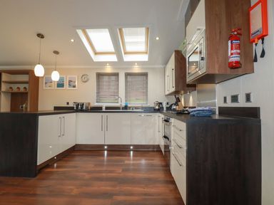 A kitchen with wooden floor white cabinets black counters skylights and windows at Haven Lodge in Bossiney Bay near Tintagel