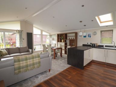 An open plan living room and kitchen with sofas, dining table, and kitchen island at Haven Lodge in Bossiney Bay near Tintagel