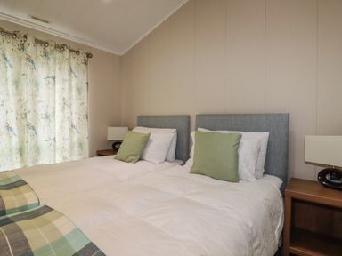 A bedroom with two single beds with green pillows and a bedside table with a lamp at Haven Lodge in Bossiney Bay near Tintagel