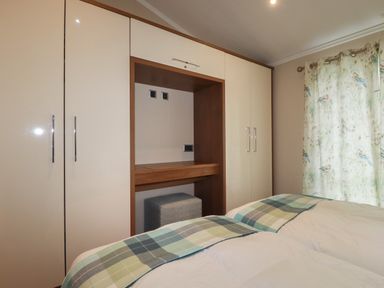 A bedroom with wardrobe cabinets bed with plaid blankets and floral curtains at Haven Lodge in Bossiney Bay near Tintagel