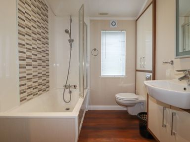 A bathroom with a bathtub and shower on the left a toilet under a window and a sink with a mirror on the right at Haven Lodge Bossiney Bay near Tintagel