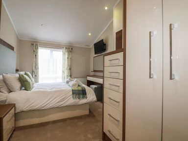 A bedroom with a bed towels on the bed a wardrobe a chest of drawers and a television at Haven Lodge in Bossiney Bay near Tintagel