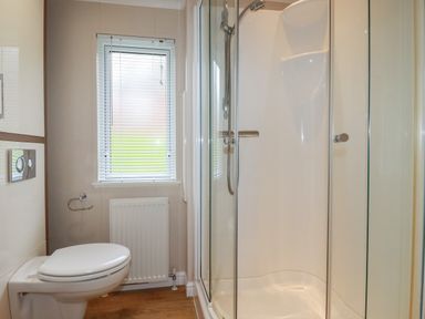 A bathroom with a toilet a window and a glass enclosed shower at Haven Lodge in Bossiney Bay near Tintagel