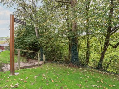 A grassy area with trees and a wooden signpost showing direction to Halgabron and Waterfall at Haven Lodge in Bossiney Bay near Tintagel