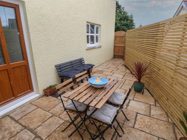 A small outdoor patio with a wooden table and chairs a bench and potted plants at The Loft @ Wisteria Cottage Saundersfoot