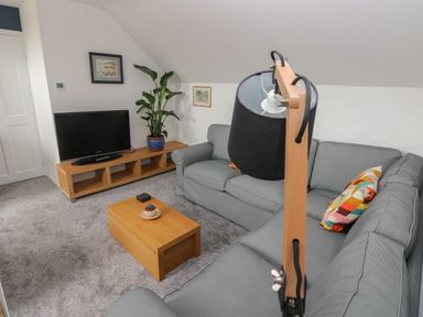 A living room with gray sofas a wooden coffee table a flat screen tv on a wooden stand and a floor lamp at The Loft @ Wisteria Cottage in Saundersfoot