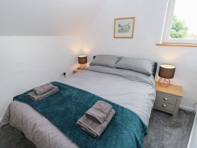A bedroom with a double bed two bedside tables with lamps a window and a framed picture on the wall at The Loft @ Wisteria Cottage in Saundersfoot