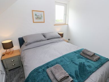 A bedroom with a bed with gray bedding and teal blanket with towels bedside tables with lamps and a window at The Loft @ Wisteria Cottage in Saundersfoot